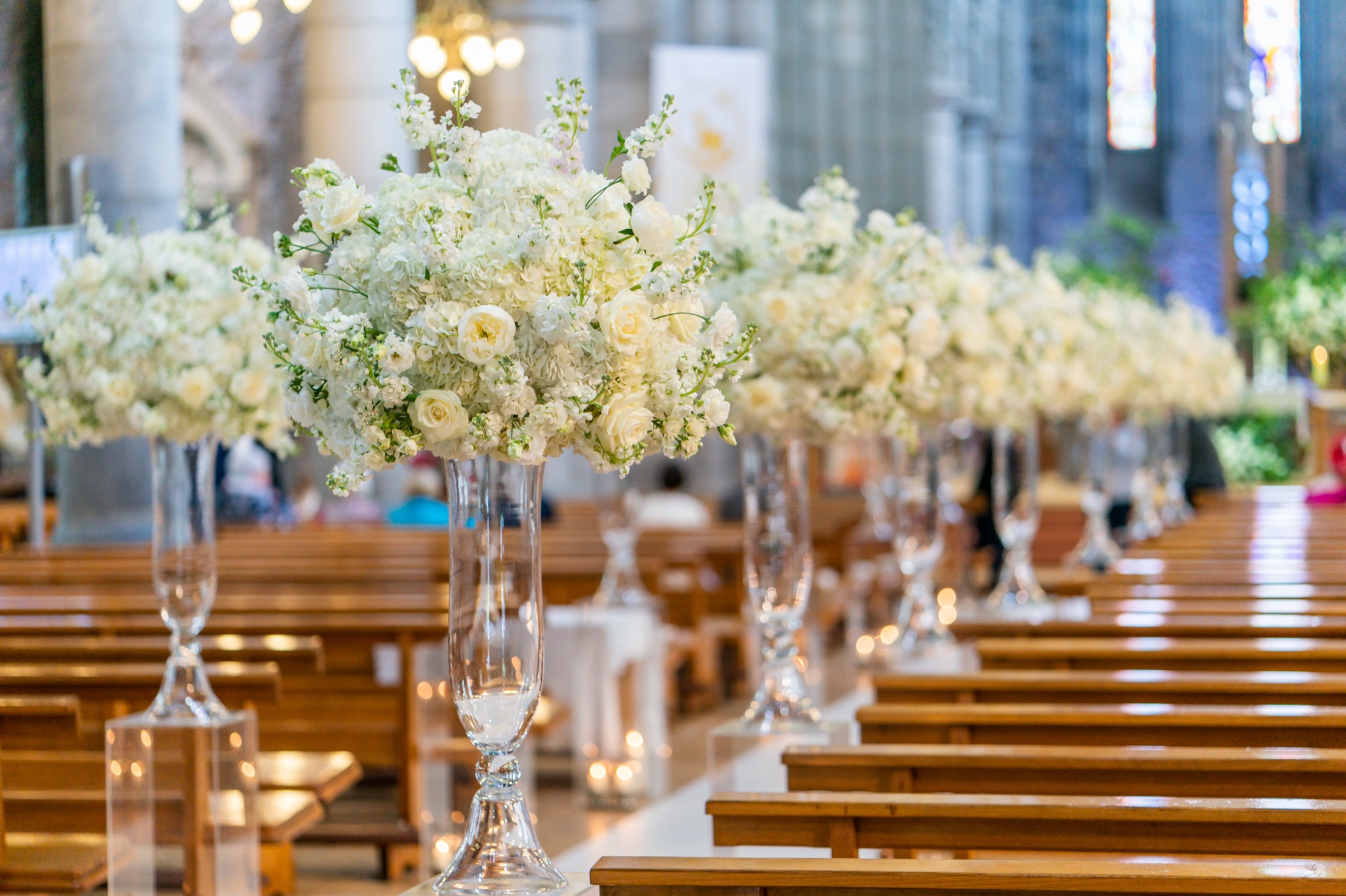 Church aisle lined with white floral arrangements and candles